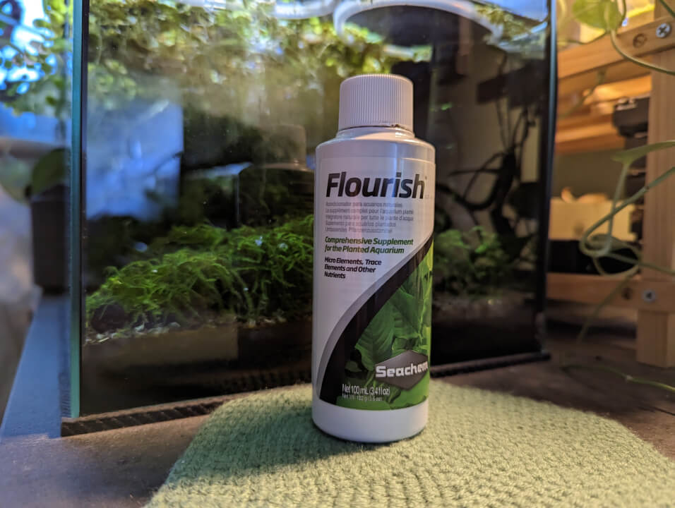 A bottle of Seachem Flourish in front of a planted shrimp tank